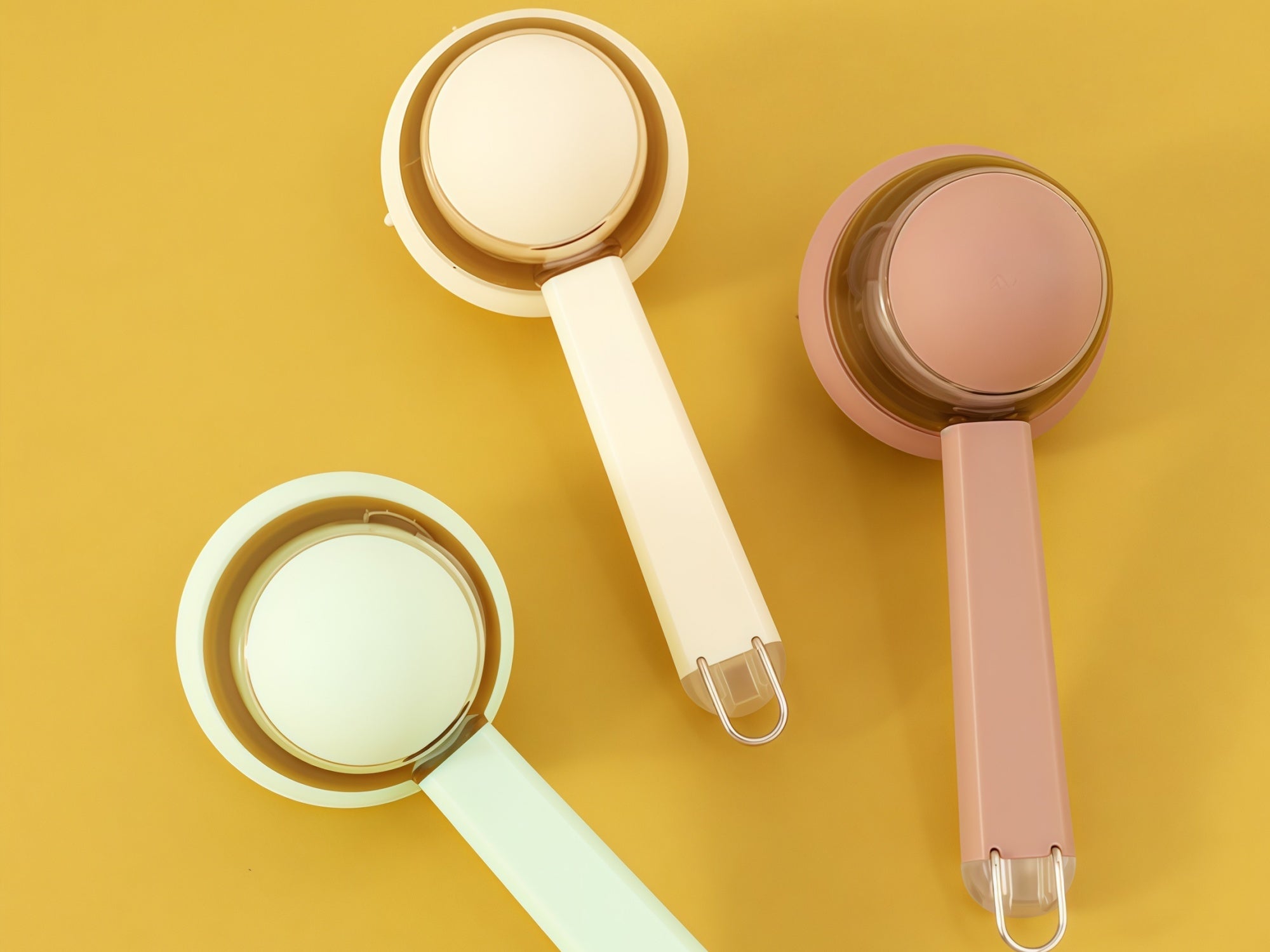 Three measuring cups in beige, pink, and green on a yellow background